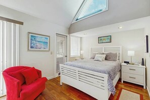 Une chambre à coucher avec un lit, une table de chevet, un fauteuil rouge et un tableau accroché au mur.
