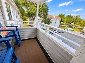 A balcony with a view of a street and parked cars, a blue chair, and a white railing. - Arcadian Dunes 18-370 (Myrtle Beach)