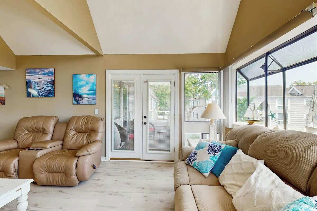 Un salon avec un canapé beige, un fauteuil inclinable et une porte vitrée donnant sur l’extérieur.