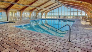 An indoor swimming pool with a brick floor, wooden ceiling, and large windows. - Sands Ocean Club 1629 (Myrtle Beach)