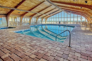 Ein Hallenbad mit Ziegelboden, Holzbalkendecke und großen Fenstern.