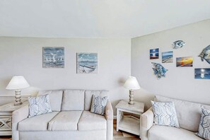 A room with two sofas, a small table, and wall art depicting maritime scenes. - Sands Ocean Club 1629 (Myrtle Beach)