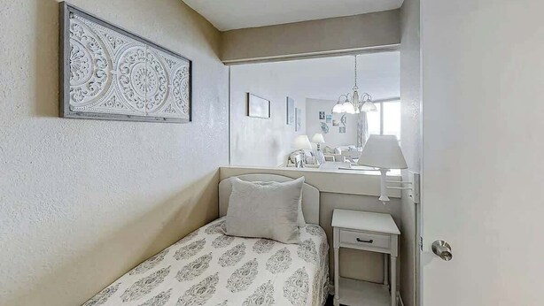 A bedroom with a bed, a bedside table, a nightstand, a mirror, and a decorative wall piece. - Sands Ocean Club 1629 (Myrtle Beach)