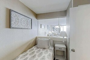 A bedroom with a bed, a bedside table, a nightstand, a mirror, and a decorative wall piece. - Sands Ocean Club 1629 (Myrtle Beach)