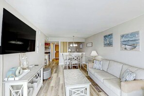 A modern living room with a sofa, a coffee table, a TV, and a dining area with a table and chairs. - Sands Ocean Club 1629 (Myrtle Beach)