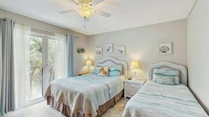 Een slaapkamer met twee bedden, een plafondventilator en een groot raam met gordijnen.