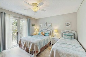 Ein Schlafzimmer mit zwei Betten, einem Deckenventilator und einem großen Fenster mit Vorhängen.