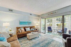 Ein Wohnzimmer mit einer Couch, einem Hocker und einem Gemälde von einer Strandansicht.