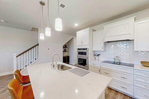 A modern kitchen with white cabinetry, a marble island, and pendant lighting. - Double Eagle Escape Retreat (North Myrtle Beach)