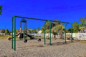 A playground with swings and a slide, surrounded by a fence and trees. - Fairway Oaks Unit 24B (North Myrtle Beach)