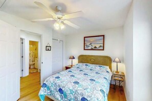 A bedroom with a bed, a ceiling fan, a nightstand, a lamp, a framed picture on the wall, and a door leading to another room. - Fairway Oaks Unit 24B (North Myrtle Beach)