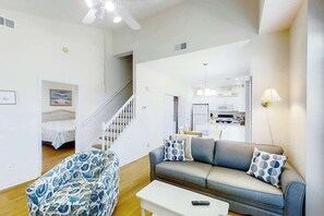 A modern living room with a sofa, a patterned armchair, and a white coffee table. A staircase leads to an upper level. - Fairway Oaks Unit 24B (North Myrtle Beach)
