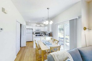 A modern kitchen with white cabinets, a dining area with a wooden table and chairs, and a large window providing natural light. - Fairway Oaks Unit 24B (North Myrtle Beach)