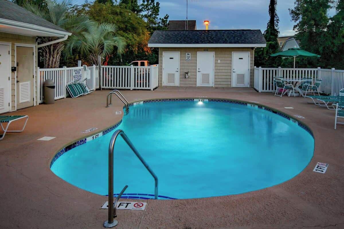 A swimming pool with a metal ladder, surrounded by a white fence, and a building with doors in the background.