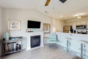 A modern living room with a fireplace, a flat-screen TV, and a kitchen area with bar stools. - Waterway Landing 205-H (North Myrtle Beach)
