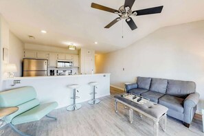 Eine moderne Küche mit einer zentralen Kochinsel, Barhocker, einem grauen Sofa und einem Deckenventilator.