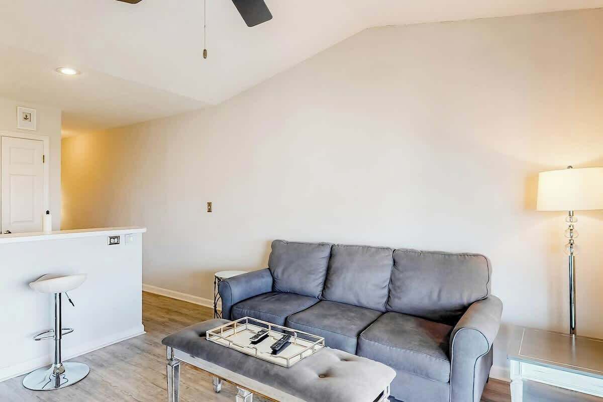 Una sala de estar con un sofá gris, una mesita blanca y un taburete.