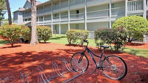 A multi-story building with a balcony on each floor, a bicycle parked in front, and a well-maintained garden with red mulch and trimmed bushes. - Renaissance Tower 908 (Myrtle Beach)