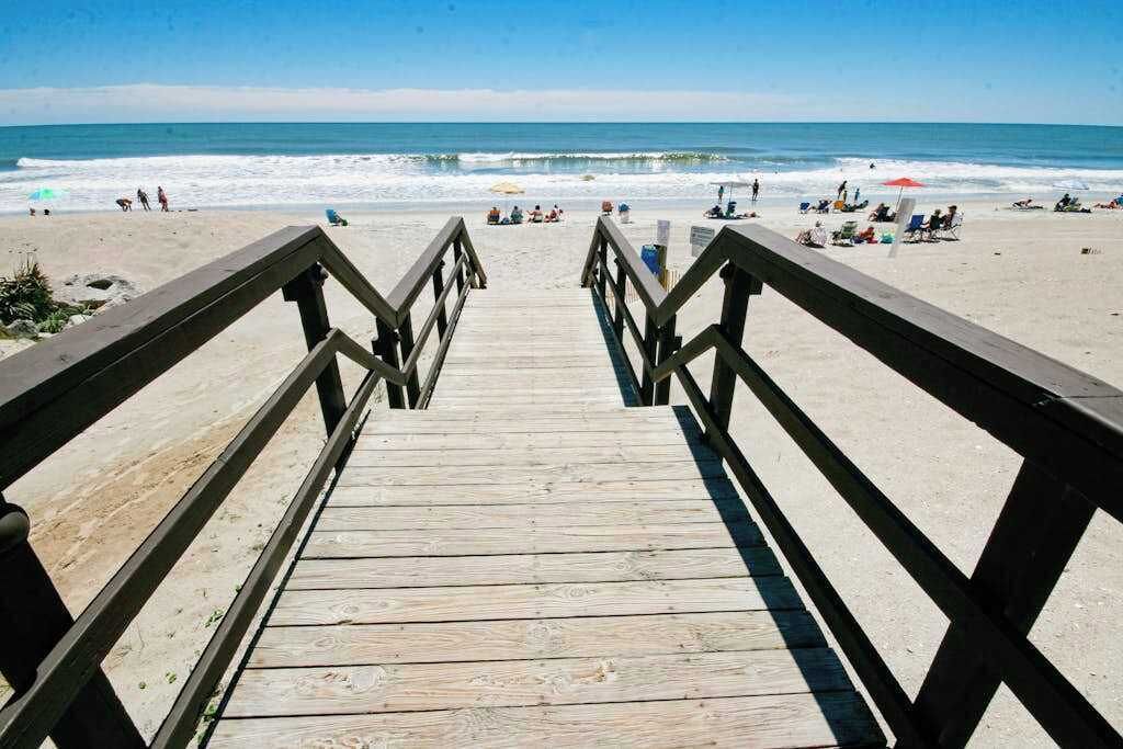 A wooden boardwalk leading to a beach with people and umbrellas.