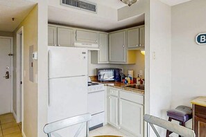 A compact kitchen with white cabinets, a built-in microwave, and a refrigerator. - Renaissance Tower 908 (Myrtle Beach)