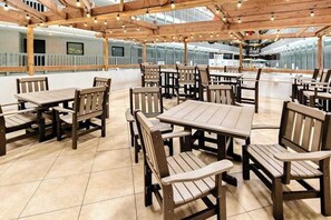 Un espace de restauration en plein air avec des tables et des chaises en bois, sous une pergola en bois agrémentée de guirlandes lumineuses.