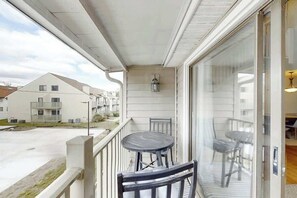 Ein Balkon mit Tisch und Stühlen, Blick auf benachbarte Gebäude und eine Glastür zu einem Innenraum.