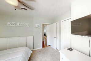 Quarto com uma cama, televisão e corredor que dá para outro espaço.