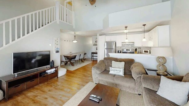 A modern living room with a flat-screen TV, a sofa, a coffee table, and a staircase. - Greystone Condos 203 (Myrtle Beach)