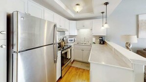 A modern kitchen with stainless steel appliances, white cabinetry, and pendant lighting. - Greystone Condos 203 (Myrtle Beach)