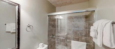 A bathroom with a shower, toilet, sink, and a large mirror.
