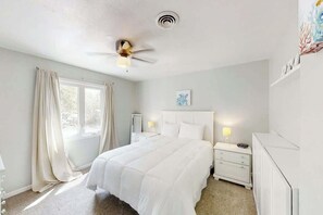 Ein Schlafzimmer mit einem Bett, Nachttischen, einem Deckenventilator und einem Fenster mit Vorhängen.