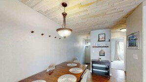 A dining area with a wooden table, white placemats, and a hanging light fixture. - Greystone Condos 203 (Myrtle Beach)