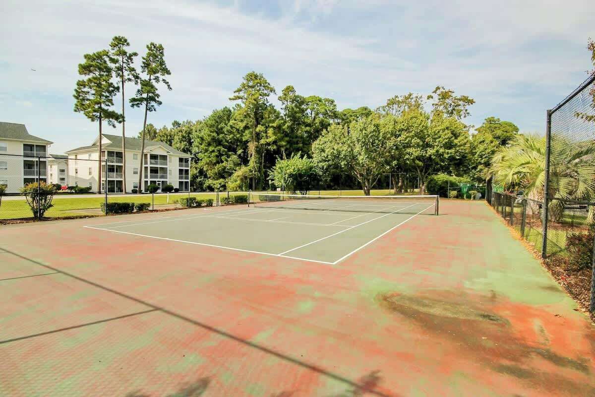 Ein Tennisplatz im Freien mit umgebender Bepflanzung und einem Gebäude im Hintergrund.