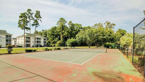 Ein Tennisplatz im Freien mit umgebender Bepflanzung und einem Gebäude im Hintergrund.