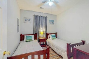 A room with two single beds, a ceiling fan, a window with curtains, and a small table with a lamp. - Shoreline Serenity at River Oaks (Myrtle Beach)