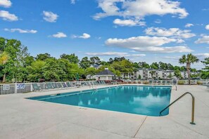 A swimming pool with a metal handrail, surrounded by a fence, with buildings and trees in the background. - Shoreline Serenity at River Oaks (Myrtle Beach)