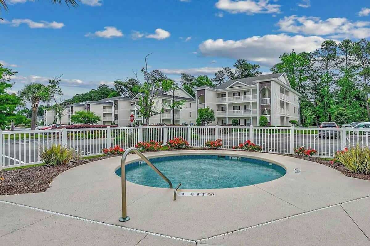A pool area with a 1.5 ft depth marker, surrounded by a white fence, with multi-story buildings in the background.