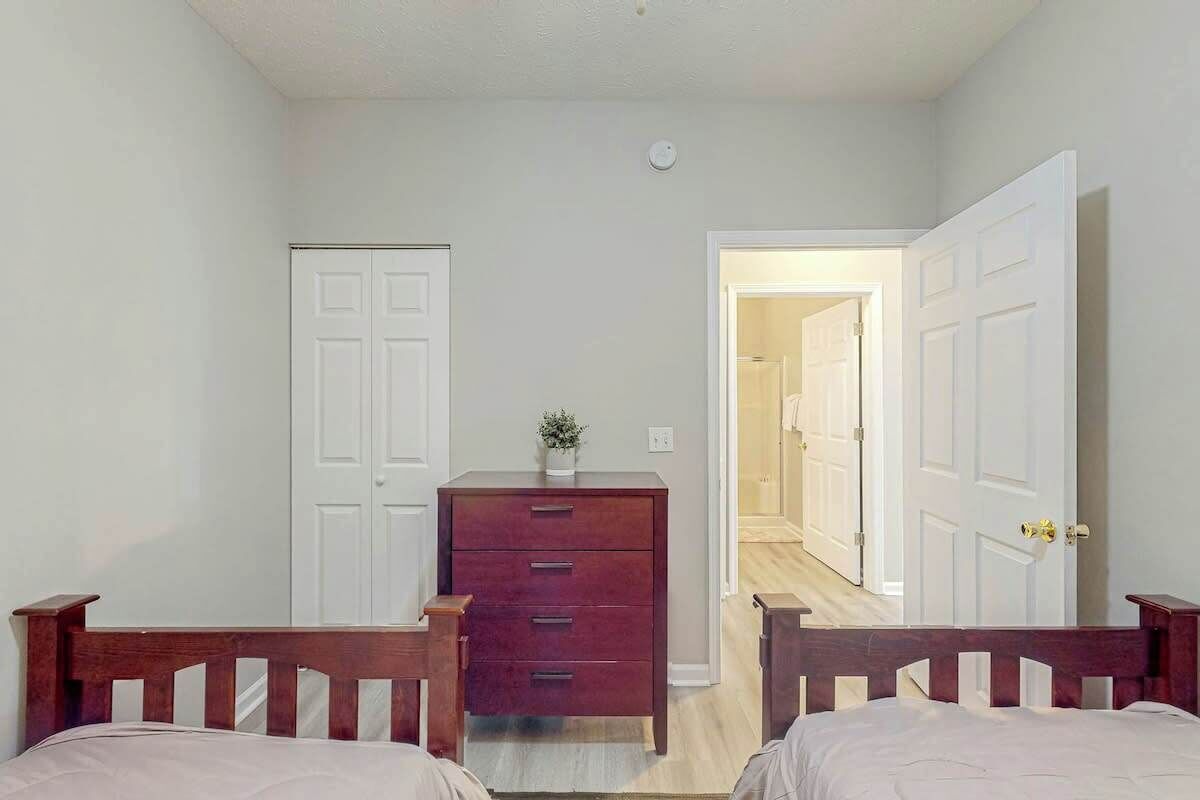 A bedroom with two beds, a dresser, and a door leading to another room.