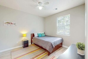 Ein Schlafzimmer mit Bett, Nachttischlampe, Fenster und Deckenventilator.