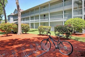 A multi-story building with a balcony on each floor, a bicycle parked in front, and a well-maintained garden with trimmed bushes. - Myrtle Beach Resort A-326 (Myrtle Beach)