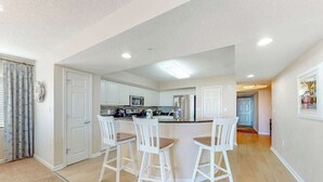 A modern kitchen with white cabinets, a central island with bar stools, and a microwave. - Yacht Club Villas 3-505 (North Myrtle Beach)