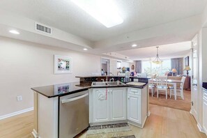 A modern kitchen with white cabinets, a dishwasher, and a dining area with a table and chairs. - Yacht Club Villas 3-505 (North Myrtle Beach)