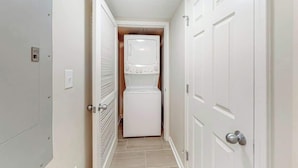 A laundry room with a stacked washer and dryer, a metal utility cabinet, and a door with a handle. - Yacht Club Villas 3-505 (North Myrtle Beach)