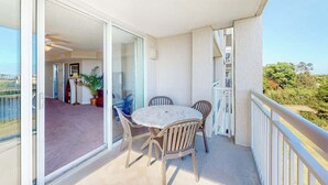 An open balcony with a table and chairs, a sliding glass door leading to an interior space, and a view of greenery. - Yacht Club Villas 3-505 (North Myrtle Beach)