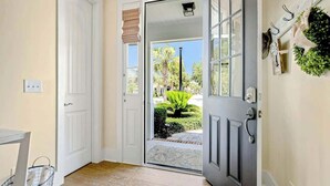 A hallway with a door leading to a garden view, a small table, and a basket. - Barefoot Livin' Retreat (North Myrtle Beach)