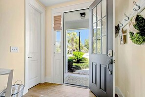 Um corredor com porta que dá para um jardim, uma pequena mesa e um cesto.