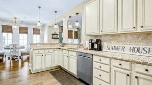 A spacious kitchen with white cabinetry, a granite countertop, and a sign reading 'SUMMER HOUSE'. - Barefoot Livin' Retreat (North Myrtle Beach)