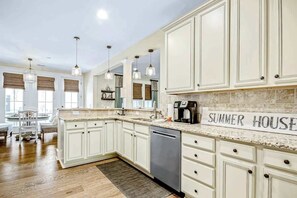 Uma cozinha espaçosa com armários brancos, bancada de granito e uma placa indicando 'SUMMER HOUSE'.