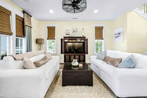 A living room with two white sofas, a coffee table, a television, and a ceiling fan. - Barefoot Livin' Retreat (North Myrtle Beach)