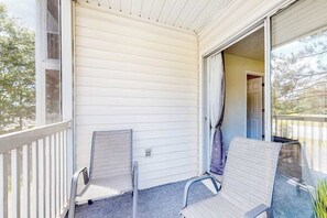 A covered porch with two chairs and a sliding glass door leading to an interior room. - River Oaks 40D 2BR Condo (Myrtle Beach)